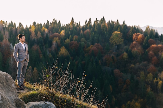 Novio en traje de pie y mirando la puesta de sol en el fondo de la montaña de roca superior Boda de otoño