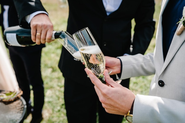 El novio vierte champán en una copa en el fondo de los amigos en la naturaleza en la ceremonia de la boda Cerrar Brindis