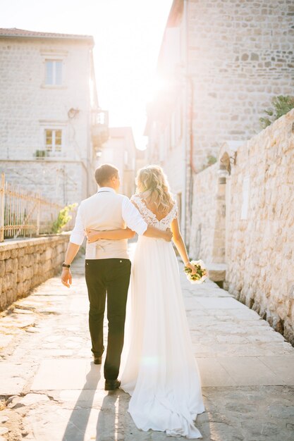 Los novios se abrazan por las calles de Perast junto a casas de ladrillo blanco.