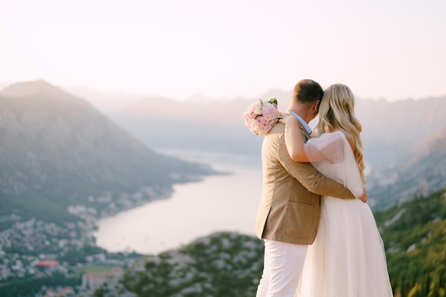 Los novios se abrazan en la montaña y miran la bahía