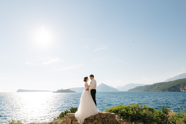 Los novios se abrazan en la playa de la isla Mamula con el telón de fondo de la fortaleza de Arza.