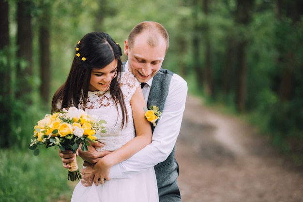 Novios abrazándose el día de la boda, feliz pareja joven besándose en el parque en la naturaleza, día de san valentín