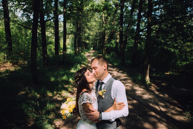 Novios abrazándose el día de la boda, feliz pareja joven besándose en el parque en la naturaleza, día de san valentín