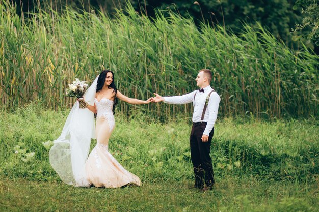 Novios abrazándose el día de la boda, feliz pareja joven besándose en el parque en la naturaleza, día de san valentín