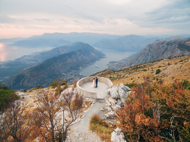 Los novios abrazándose en la plataforma de observación en el monte lovcen con vistas a la bahía de kotor