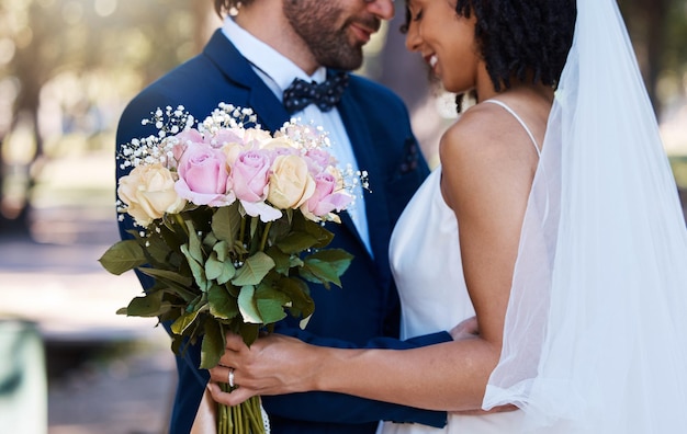 Novios y abrazo con ramo de flores al aire libre en el evento de celebración del matrimonio para la novia y el novio Feliz hombre y mujer interraciales en la ceremonia con asociación de confianza y juntos por compromiso