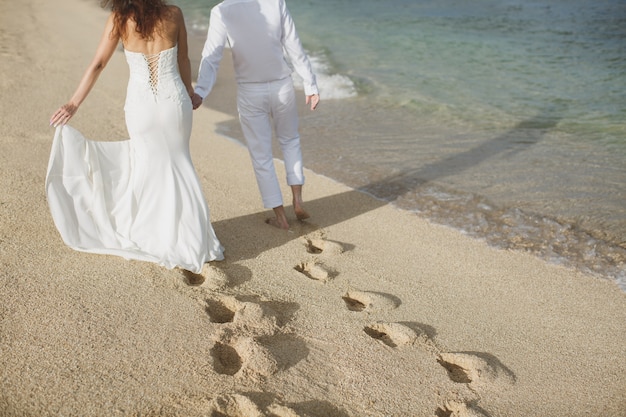 Los novios caminan de la mano en la arena. huellas en la arena cerca del mar