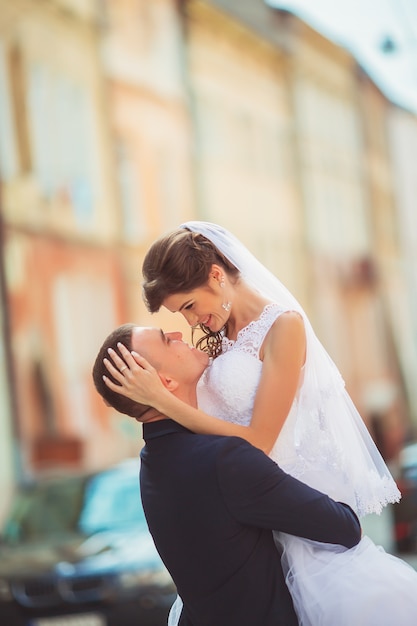 Foto novios caminando alegremente en el paisaje urbano. novia y el novio abrazándose y besándose. personas enamoradas. calles de la ciudad. día de la boda. foto horizontal en color.