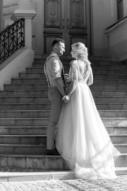 Novios en la ciudad en un día soleado de verano. la novia y el novio abrazándose en las escaleras. en blanco y negro