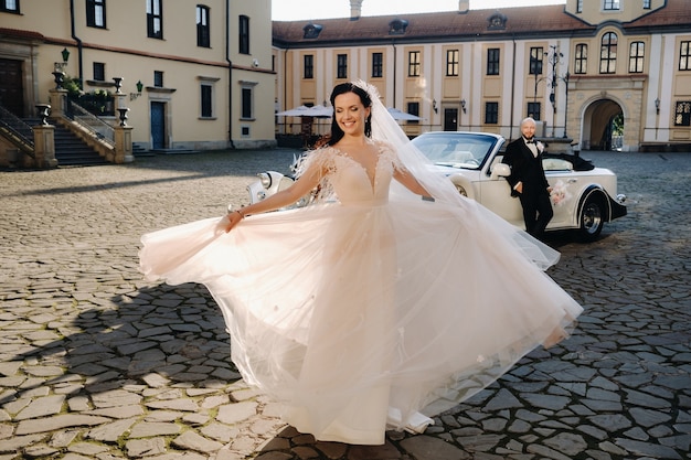 Novios elegantes en el patio del castillo cerca de un coche retro