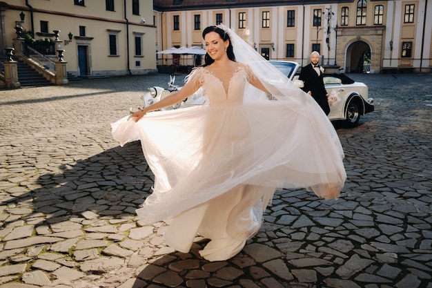 Novios elegantes en el patio del castillo cerca de un coche retro