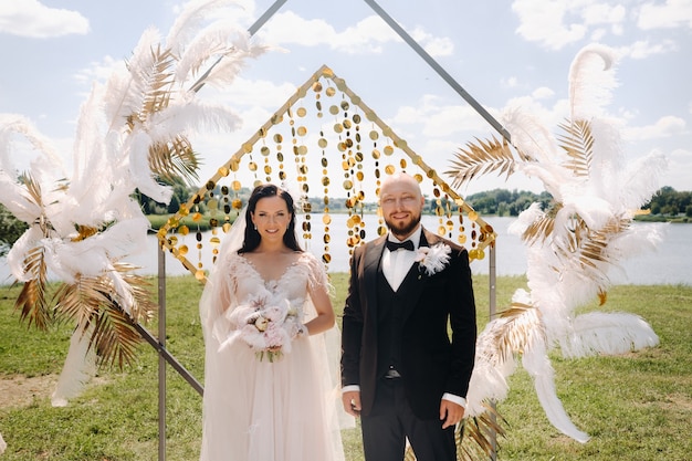 Novios felices cerca del arco durante la ceremonia de la boda.