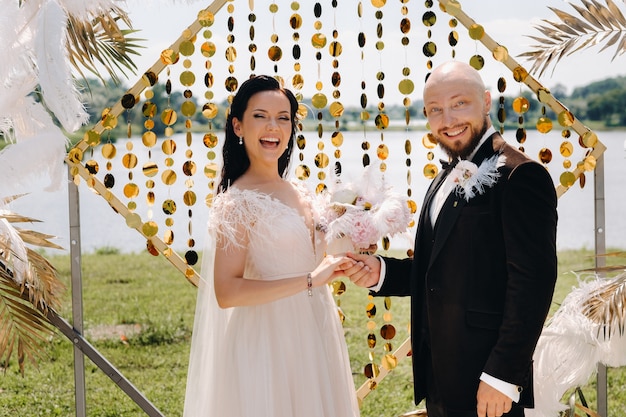 Novios felices cerca del arco durante la ceremonia de la boda.