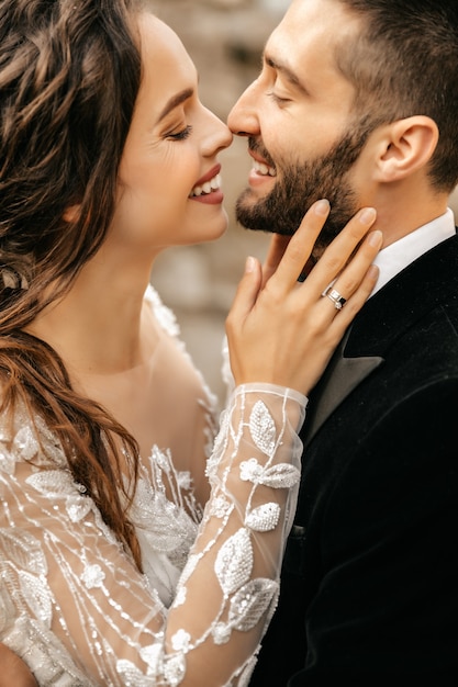 Los novios hermosos se ríen y se besan en el fondo de piedras.