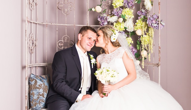 Novios en el interior se abrazan. Chica modelo hermosa en vestido blanco. Hombre de traje. Novia de belleza con el novio. Retrato femenino y masculino. Mujer con velo de encaje. Linda dama y chico guapo