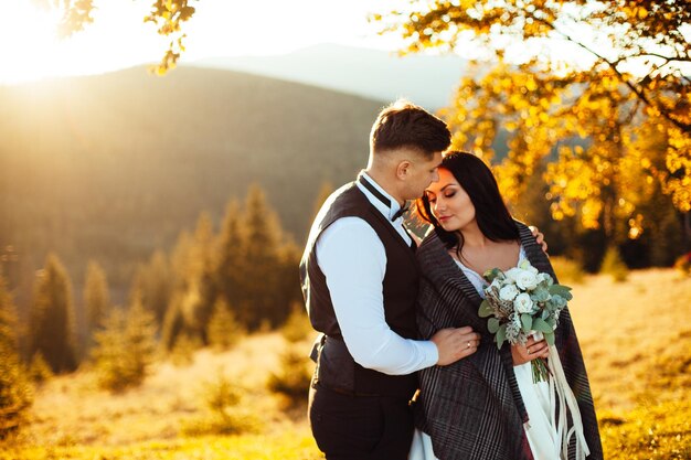 Los novios miran la puesta de sol de pie en la colina