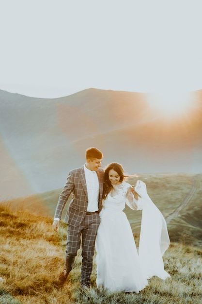 Novios sensuales novios y novias con un largo vestido blanco parados al borde de las montañas