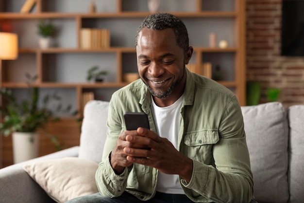 Foto novo dispositivo e aplicativo retrato de homem afro-americano sorridente de meia-idade lê mensagem no telefone assiste a vídeo