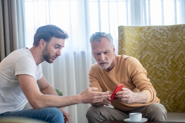 Novo dispositivo. jovem ensinando seu pai a usar um novo smartphone