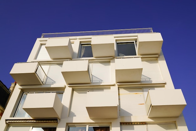 Novo edifício moderno de fachada branca com varanda quadrada e terraço cúbico no céu azul