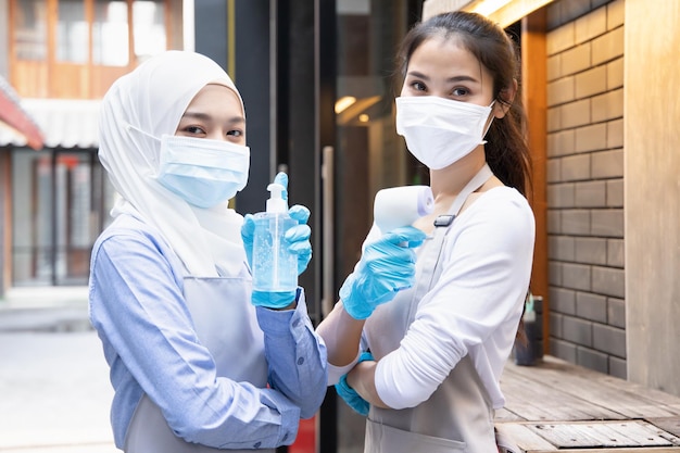 Foto novo funcionário de negócios normal ou lojista equipado com dispositivo de varredura térmica portátil e gel desinfetante para as mãos para lavagem das mãos desinfetante sem água