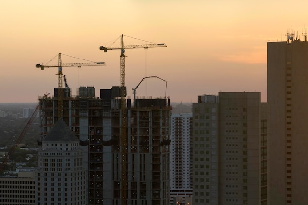 Novo local de construção de residência em desenvolvimento na área urbana americana ao pôr do sol Guindastes industriais de elevação de torre em Miami, Flórida Conceito de crescimento habitacional nos EUA