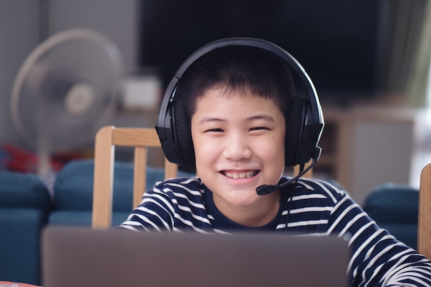 Foto novo normal menino asiático estudar online olhando para o sorriso feliz do laptop de tela e rir com diversão em casa. conceito de educação em tecnologia, trabalhar em casa