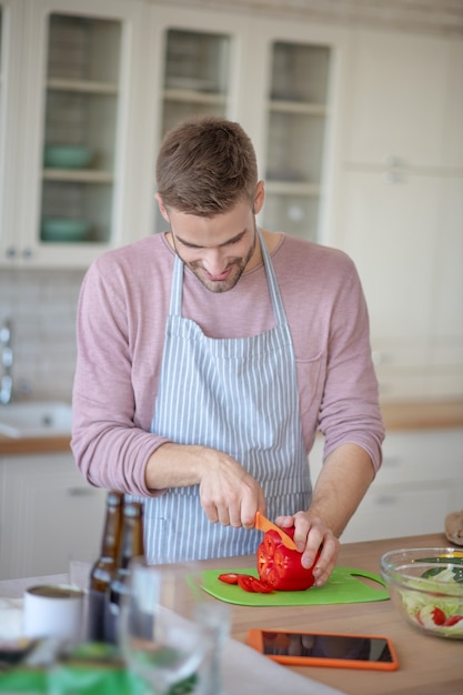 Novo prato. Um homem sorrindo picando uma pimenta vermelha fresca para um prato delicioso