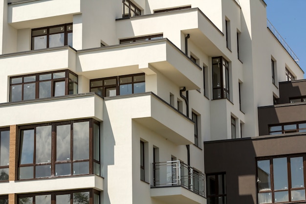 Novo prédio de apartamentos com varandas, janelas brilhantes e baixa cerca protetora no telhado plano.