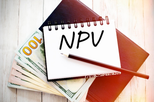 NPV-Text geschrieben auf Notizbuch mit Dollarnoten und Bleistift Finanzkonzept