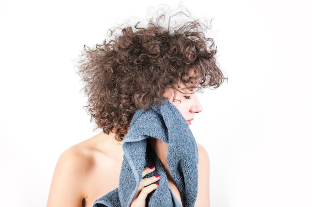 Foto nu jovem mulher com cabelo encaracolado enxuga o rosto com uma toalha contra o pano de fundo branco