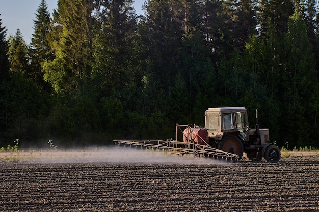 Nube de niebla creada por un pulverizador de cultivos montado en un tractor que esparce herbicidas en un campo agrícola