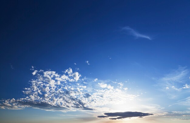 Nubes blancas y el cielo azul durante el amanecer, los colores cálidos cerca del brillo brillante a través de las nubes del sol, el paisaje