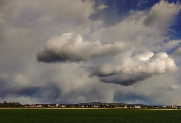 Nubes de lluvia sobre un pueblo y campos verdes frescos en primer plano