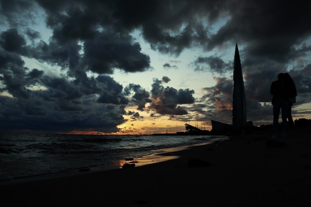 Nubes oscuras contra una puesta de sol sobre el mar, siluetas negras de personas en la orilla