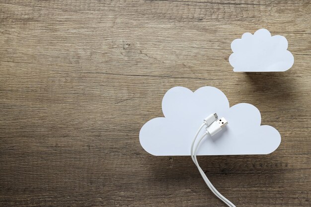 Nubes de papel blanco con un cable USB blanco en un lugar de fondo de madera para el texto