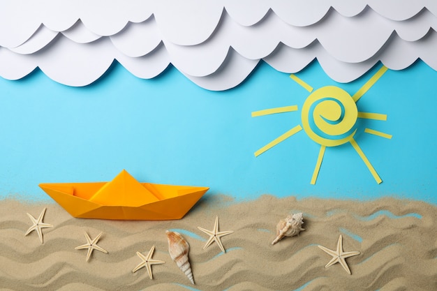 Nubes de papel, sol y barco, arena con estrellas de mar en azul. Vacaciones