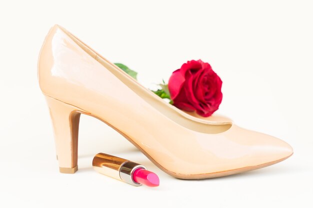 Nudefarbenes High Heels Stillleben mit roter Rosenblütenknospe und Lippenstift