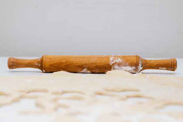 Nudelholz aus Holz, Teig und Mehl auf weißem Tisch.