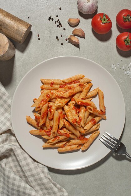 Nudeln auf einer Gabel mit Tomaten und Käse auf einem Teller auf grauem Hintergrund