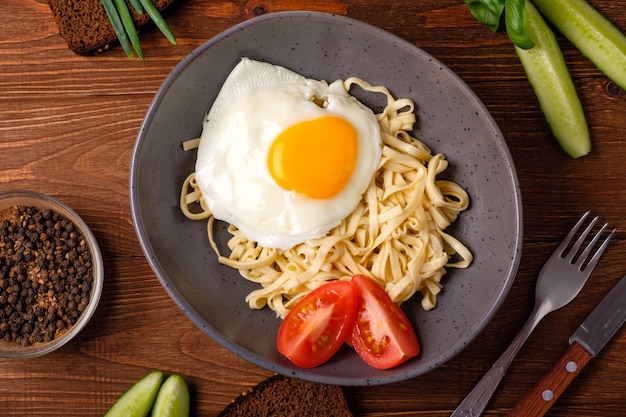 Nudeln mit Ei, Tomaten und Kräutern auf einem hölzernen Hintergrund