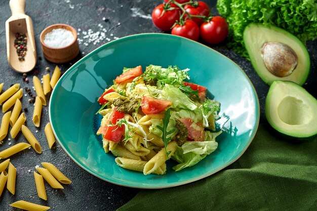 Nudeln mit Gemüse, Tomaten und Pesto auf einem Teller auf dunklem Hintergrund. Salat mit Nudeln