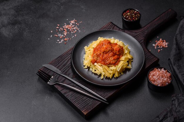 Nudeln mit Rindfleischbällchen in Tomatensauce mit Gewürzen und Kräutern auf dunklem Hintergrund