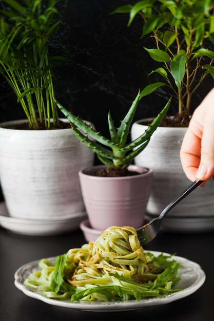 Nudeln mit Rucola und Pesto auf dem Teller. Die Hand der Frau hält die Gabel mit Spinattagliatelle