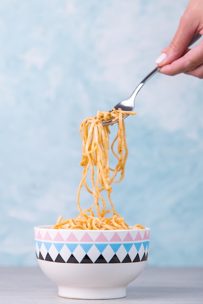Nudeln mit Sauce in einer farbigen Schüssel, Hand hält eine Gabel Nudeln hängen, Appetit Spaghetti auf blau.