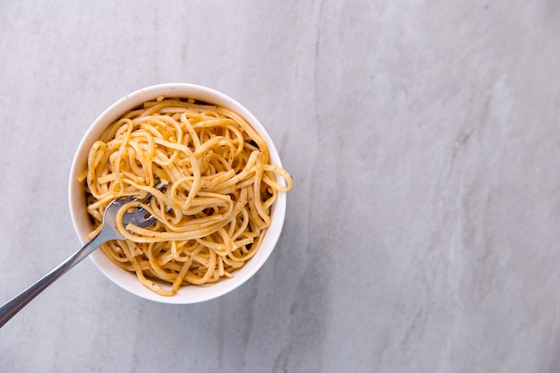 Nudeln mit Sauce in einer farbigen Schüssel mit Gabel, Appetitspaghetti auf Blau.