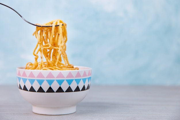 Foto nudeln mit sauce in einer farbigen schüssel mit gabel, appetitspaghetti auf blau.