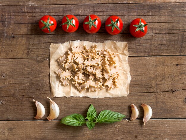 Nudeln, Tomaten, Knoblauch und Basilikum auf hölzernem Hintergrund Draufsicht