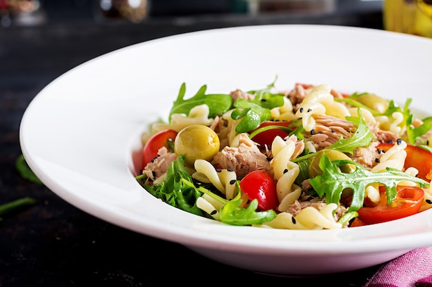 Nudelsalat mit Thunfisch, Tomaten, Oliven, Gurke, Gemüsepaprika und Arugula auf rustikalem Hintergrund.