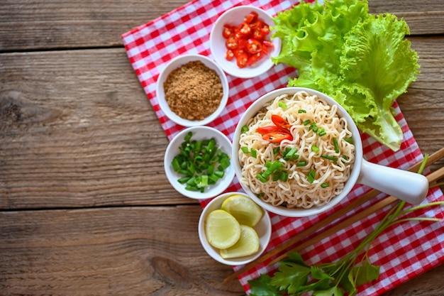 Nudelschüssel mit Gemüse, Frühlingszwiebeln, Zitrone, Limette, Salat, Sellerie und Chili auf Tischgerichten. Instant-Nudeln, die leckeres Essen mit Schüsselnudelsuppe kochen